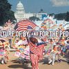 A vibrant parade on the National Mall with participants in colorful costumes, carrying flags and banners, in front of the United States Capitol building. Text is overlaid on the image that reads: Culture Of, By, and For the People