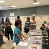 Group of adults and middle school children standing and actively discussing a set pf printed pictures laid out on a central table.