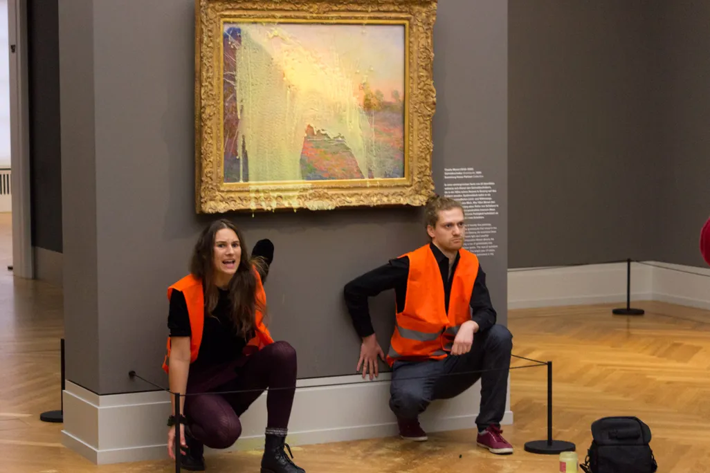 Two people with hands stuck to wall under painting smeared with potatoes