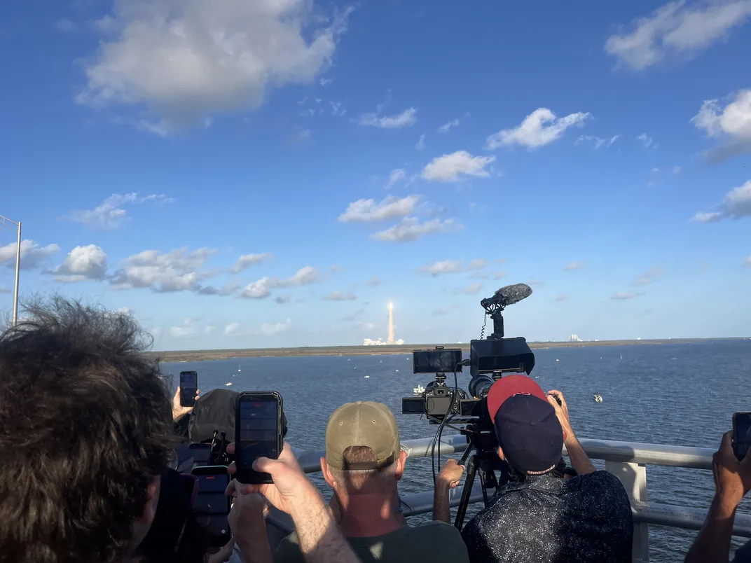 a view from behind people's heads as they take pictures of a rocket launching