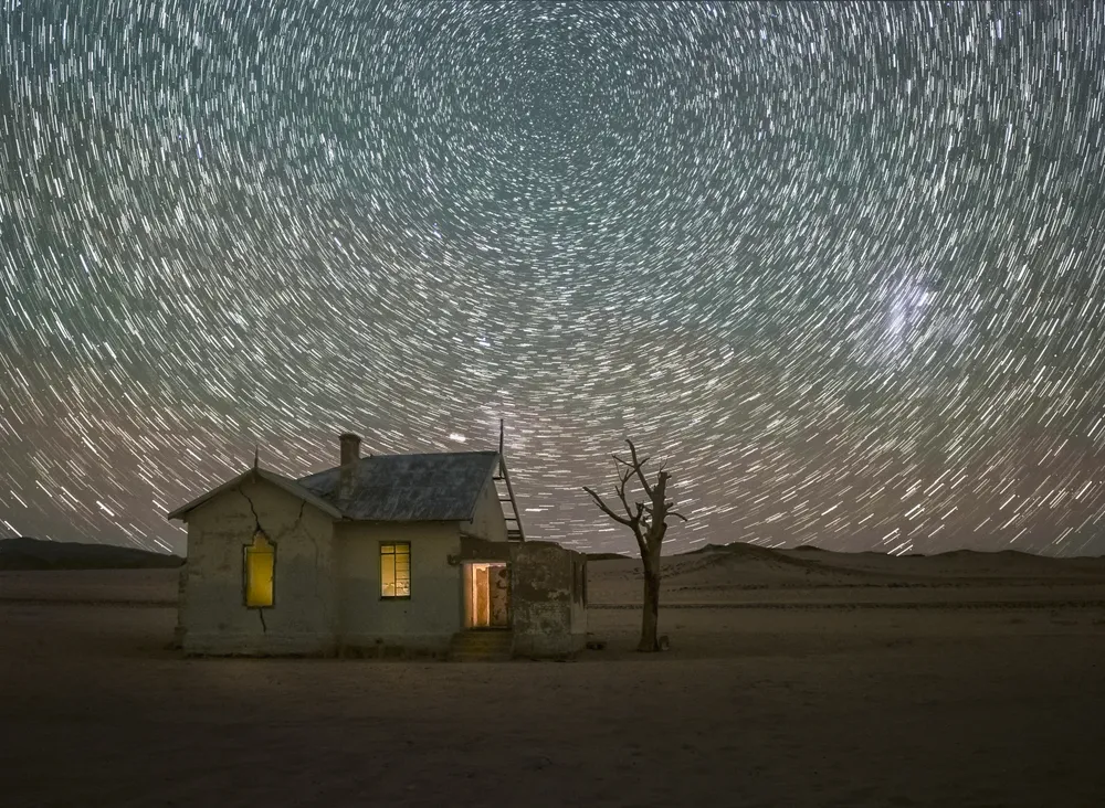 Star trails caused by the earth's rotation in this long exposure image of an abandoned house in the desert of Namibia. The Great Magellanic Cloud, a galaxy about 150,000 light years from earth, is visible as the white patch on the right. The green sky hues originate from strong air glow present during this night.