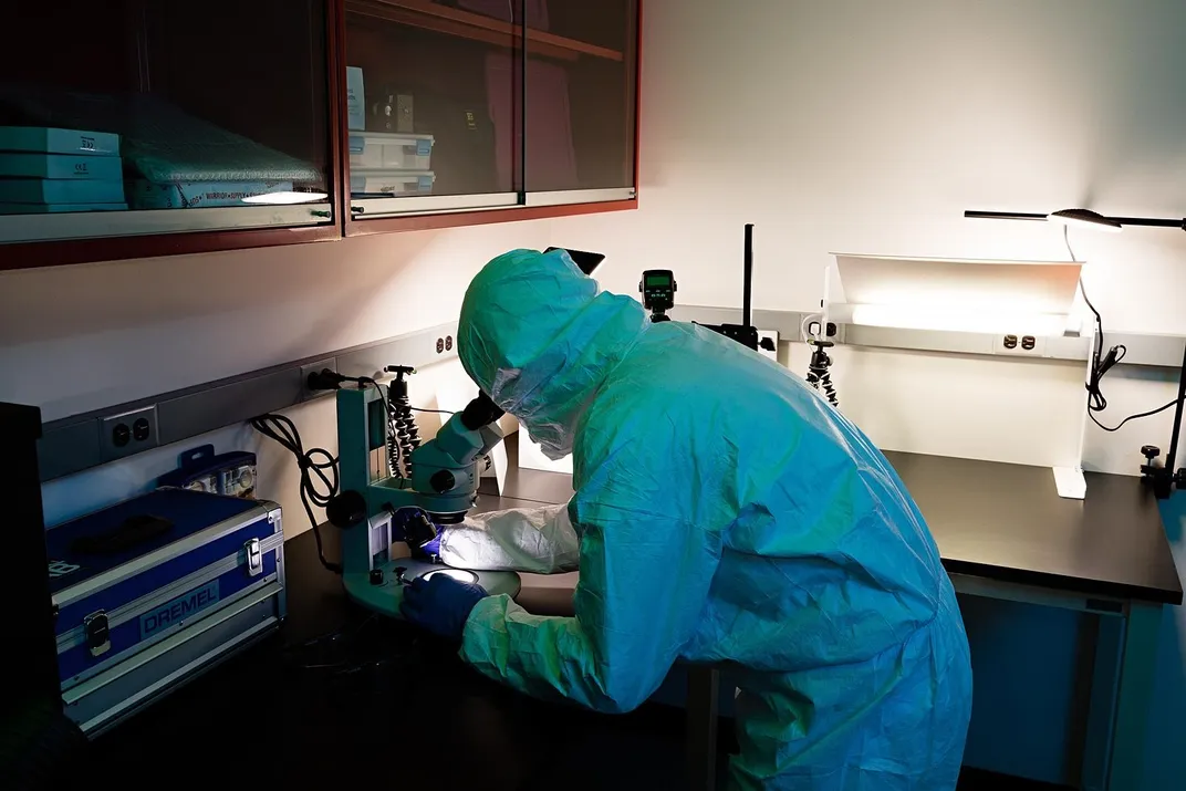 Person in a protective suit looking through a microscope.