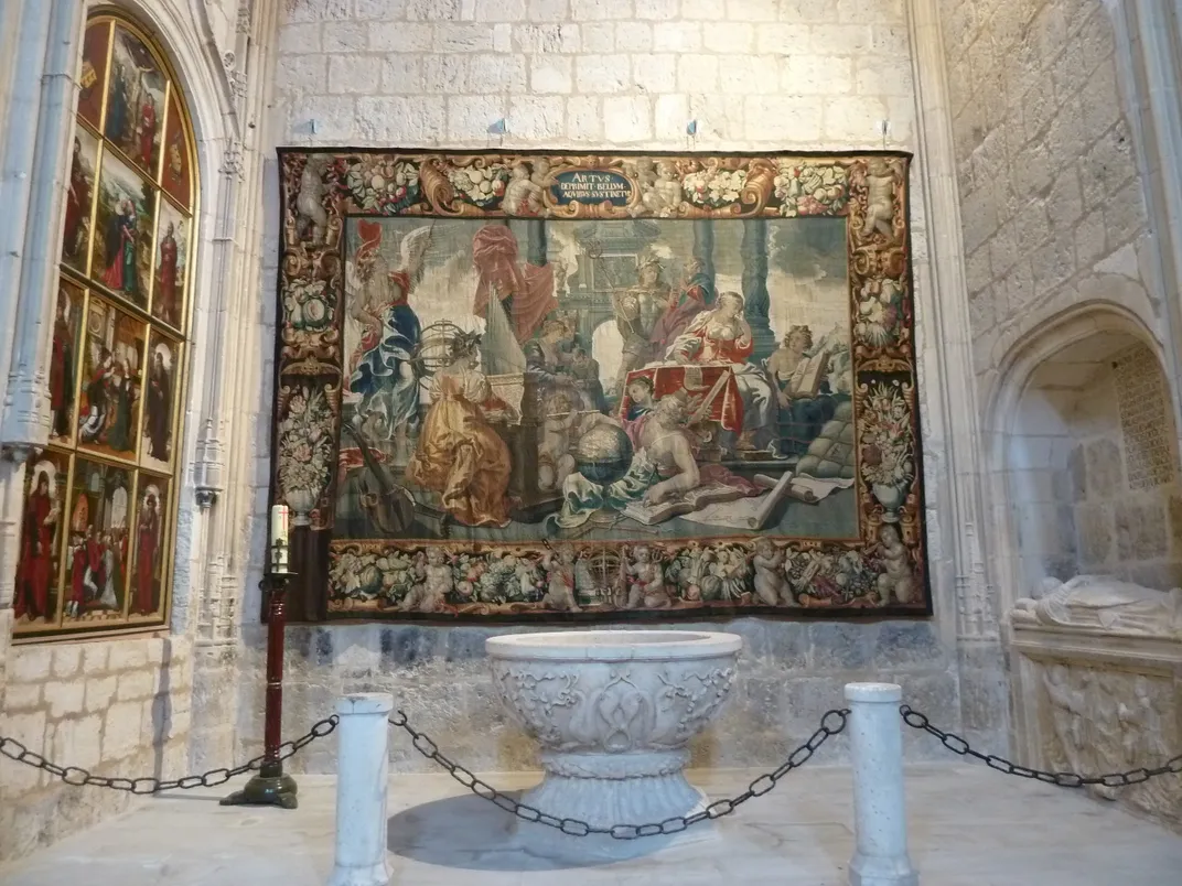 The large tapestry hangs on a stone wall in a church