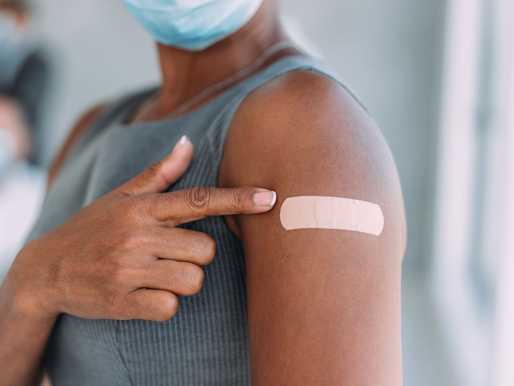 A Black woman pointing to her arm with a bandaid after vaccination