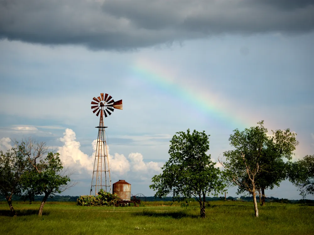 After the rain, storm clouds continue to hover above a windmill as a rainbow signals the return of the sun.