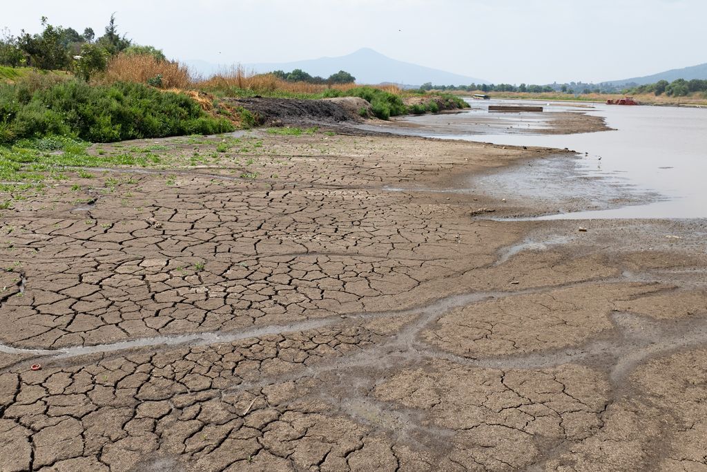 dry, cracked earth with only a little water in sight and greenery on the other side of the parched land