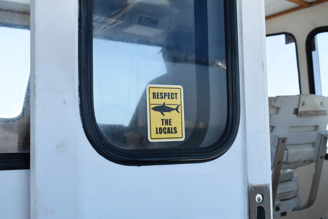 a sticker on a door on a boat says "respect the locals" with the outline of a shark