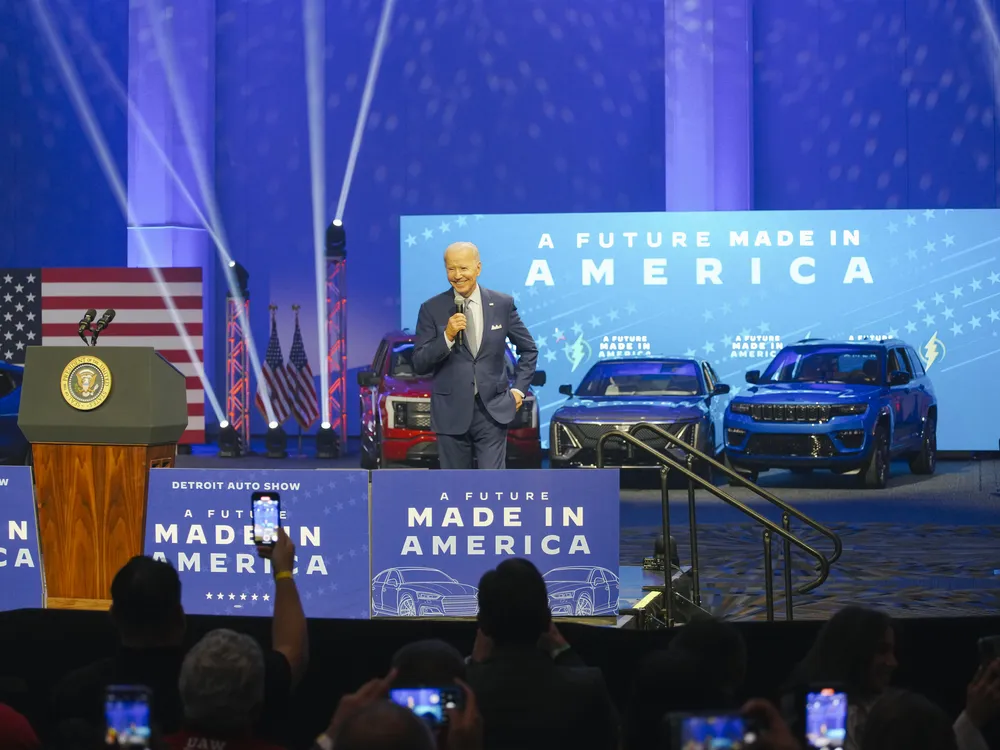 President Biden on a stage with cars and signs that read "A future made in America"