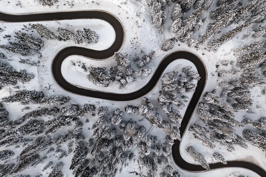 a windy road surrounded by snow-covered trees is shown from above