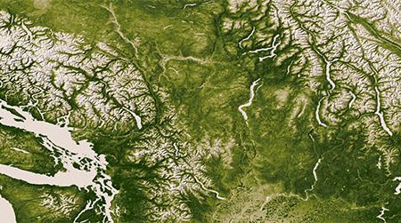 Less conspicuous than the rugged Rocky, Cascade and Coast Mountain Ranges in this photograph are the markings of agriculture, in the bottom center.