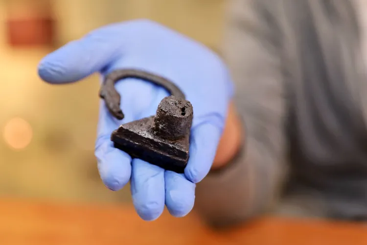 An archaeologist holds the triangular padlock found around the Polish woman's left big toe.