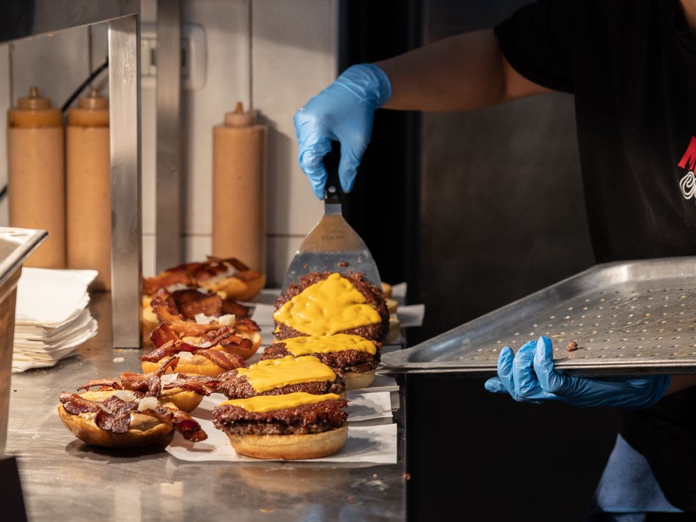 A person wearing gloves lifts burgers on to a tray