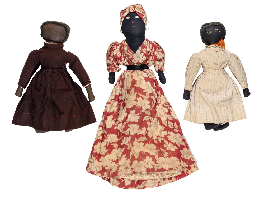 Three Black dolls of varying sizes with dresses made from dark red, patterned red flower and light pink fabrics