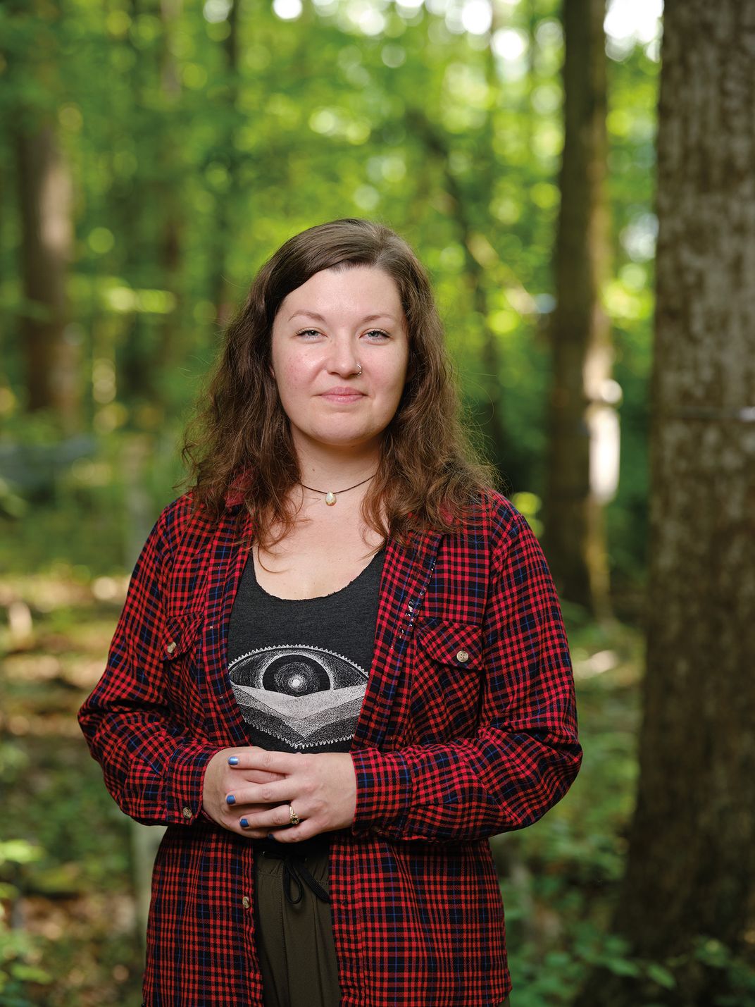 a woman in a red flannel shirt poses for a portrait in a wooded area