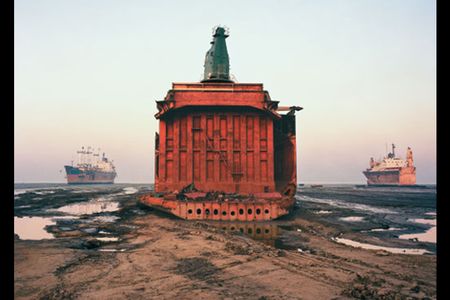 The carcass of a cargo ship, already sheared of its forward structure, sits where it was parked on the beach at Chittagong, Bangladesh, flanked by two other scrapped vessels in various states of dismemberment.