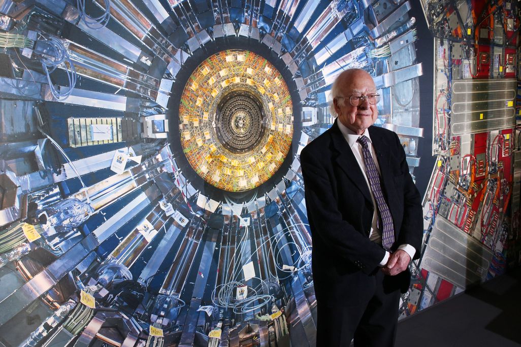 Peter Higgs stands in front of a photograph of the Large Hadron Collider