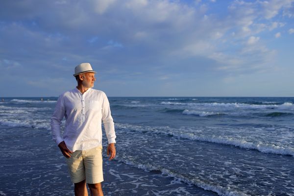 A man in a white shirt and hat on the seashore thumbnail