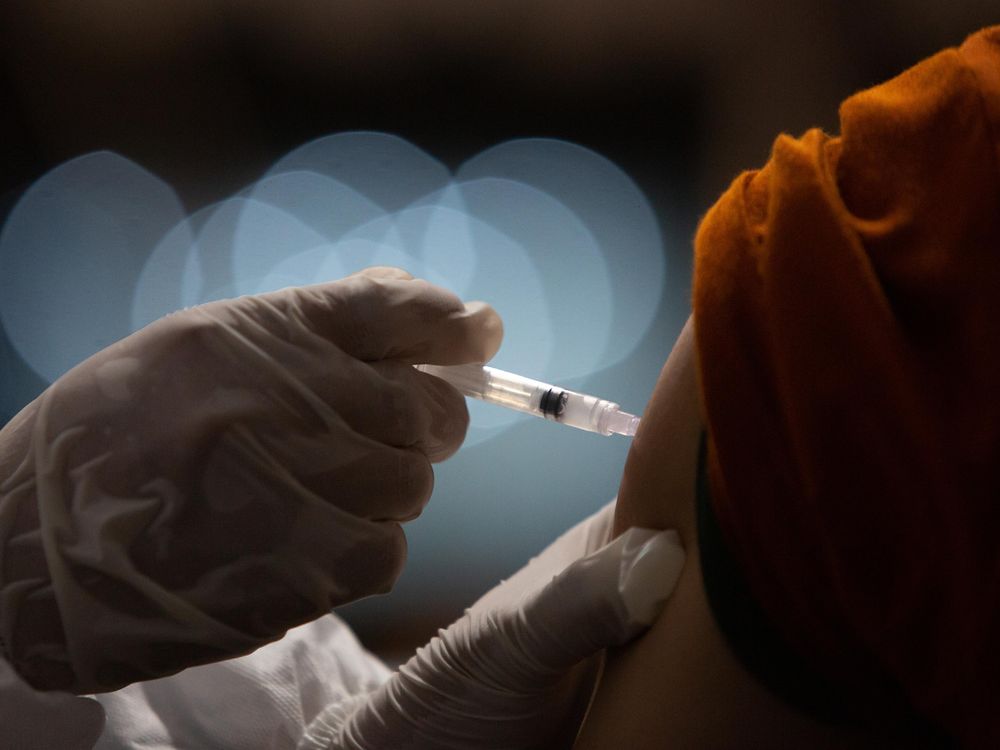 An Indonesian doctor injects a dose of Sinovac COVID-19 vaccine to a man's upper arm. 
