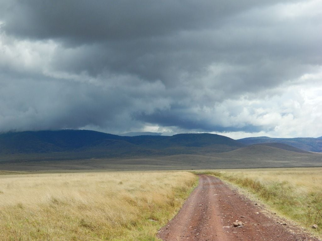 The red clay road in contrast to the bright landscape and dark clouds ...