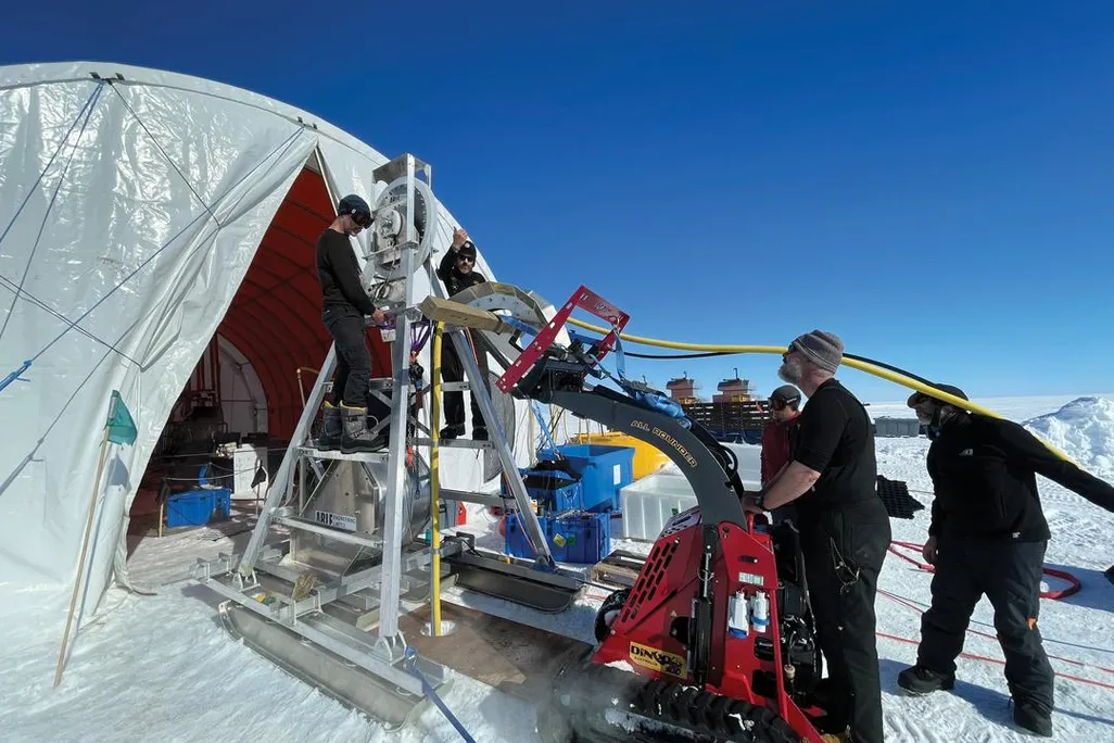 An image of reseachers gathered outside a tent using equiptment to drill a hole in ice