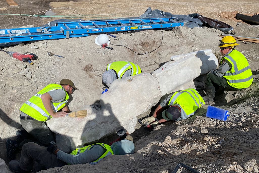 People wearing bright green vests moving a heavy object out of a hole