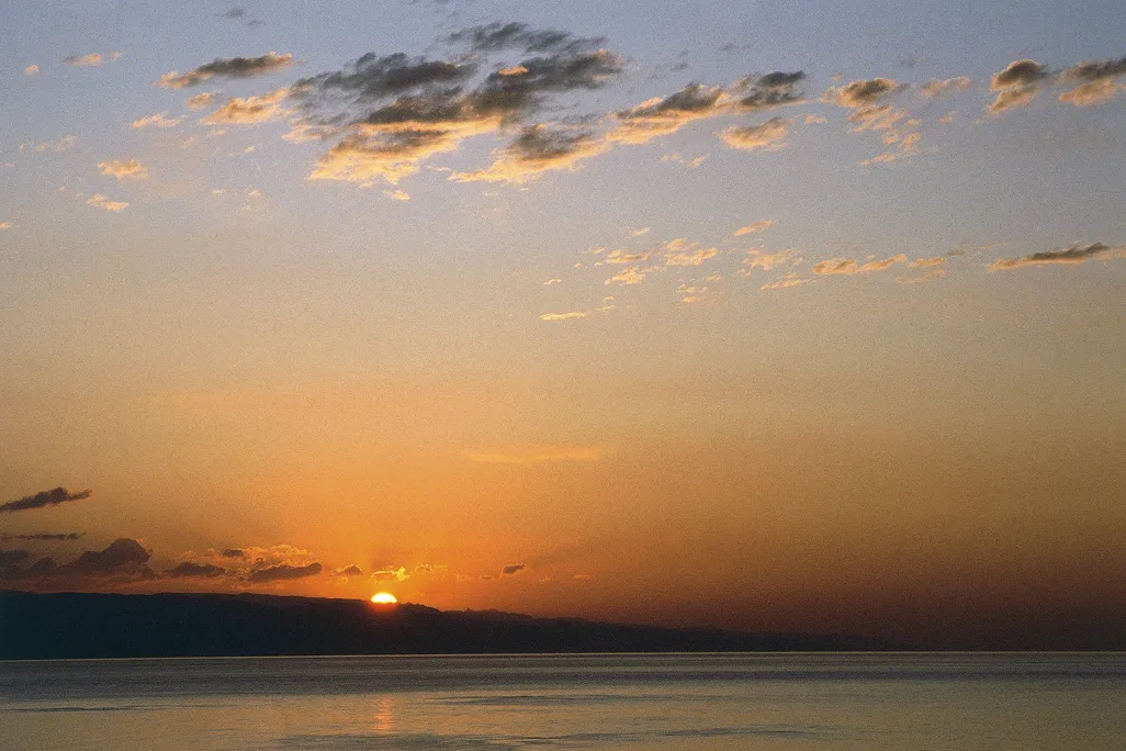a few clouds above the water with a sunset in the background