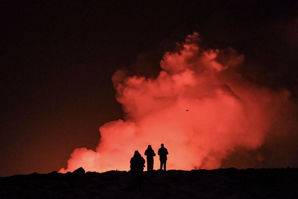 People in silhouette standing in front of a tall plume of smoke