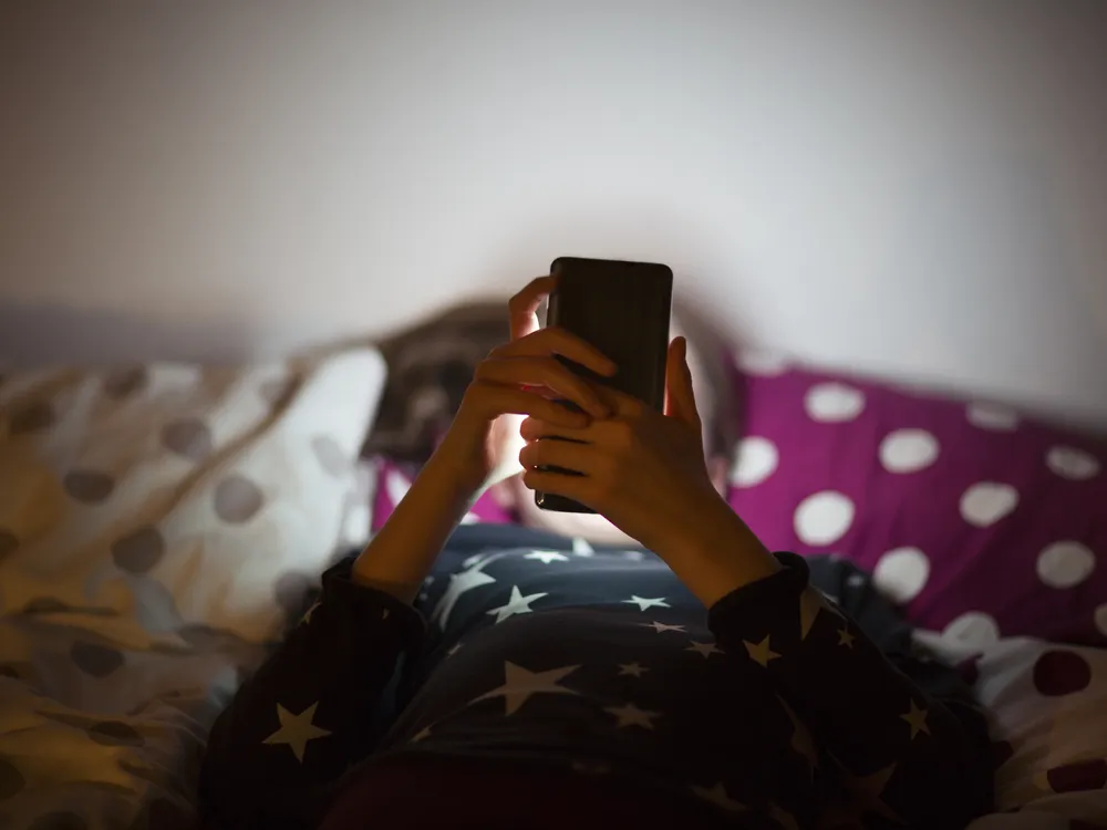 A young girl lying in bed with a phone in front of her face