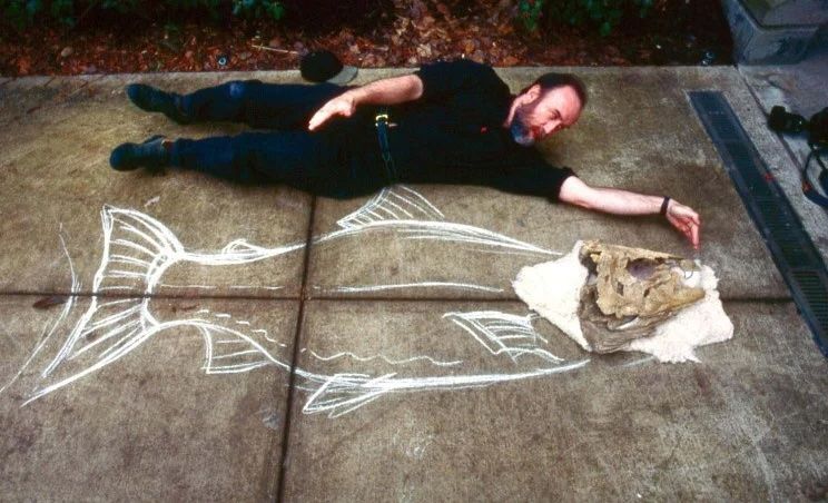 Man on the ground next to chalk drawing of salmon