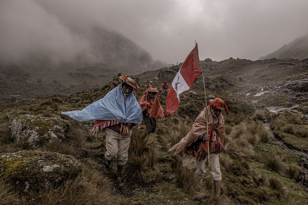 people walk in fog through mountains carrying the Peruvian flag and wrapped in cloths