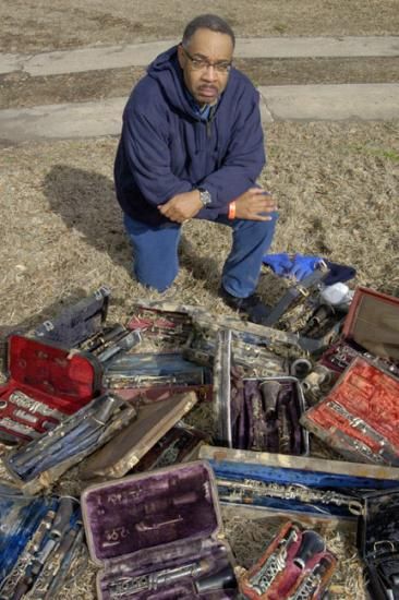 Man in sweatshirt kneels next to many ruined clarinets