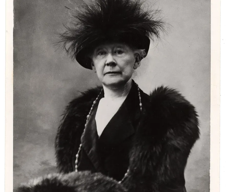 Black and white portrait of Mary Cassatt sitting in a chair wearing fur and a feathered hat.