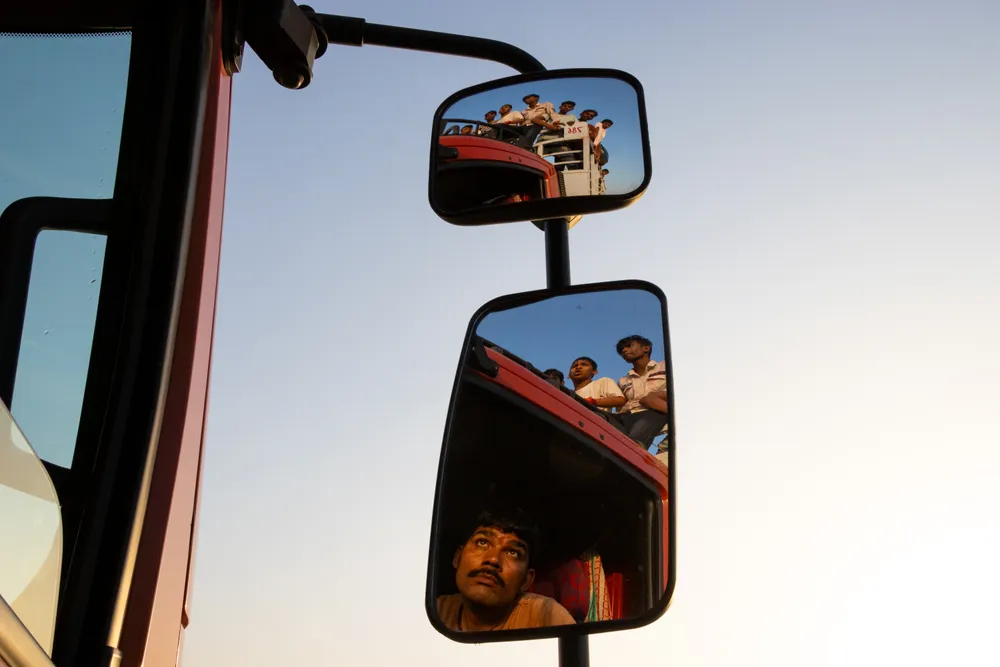 I like the focal point of the image which is a truck's mirror reflection,revealing a fascinating interplay of expressions and scenes. In the lower mirror, the driver's expression is a canvas of curiosity and amusement.He's looking at the mirror above, showing a strange sight—boys sitting on the top of the truck, happily not knowing the driver is watching them closely