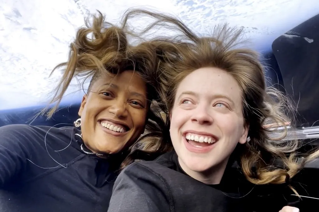 Two astronauts in space with their hair standing up and the Earth behind them