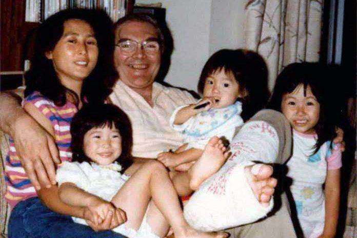 Old family photo  of mother and father and three young kids. The father has a cast on his leg, but all are smiling.