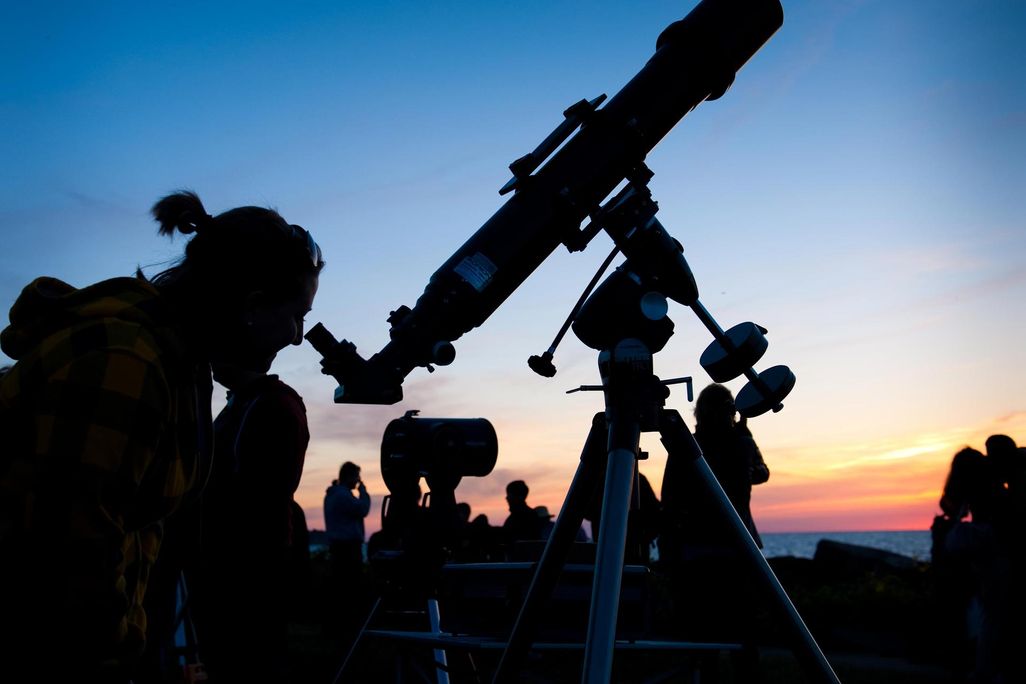 Silhouette of person looking through a telescope