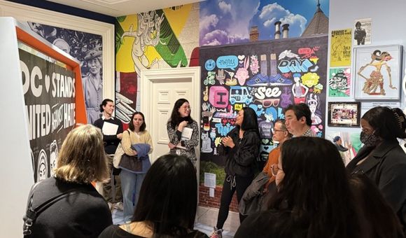 eople stand near a mural by the artist Cita Sadeli, and listen to her talking about why and how she made the mural.