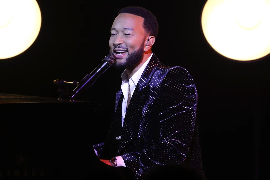 John Legend sitting at a piano singing in a microphone