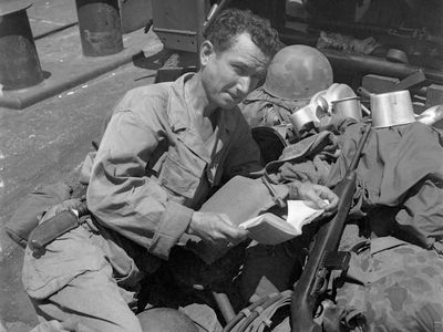 Bound for Morotai Island, Private Bryan Carroll, Memphis, TN, relaxes on the deck of an LST with a book. He leans on a pile of his belongings, which include his helmet and mess kit.
