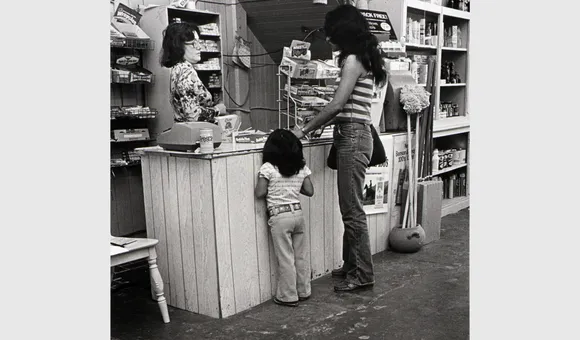 A woman and child stand at a shop counter facing a woman behind the register.