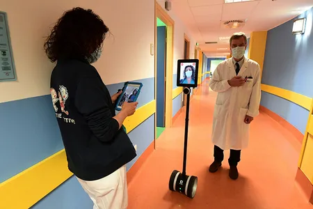 A nurse (left) operates a robot used to interact remotely with coronavirus patients while a physician looks on.