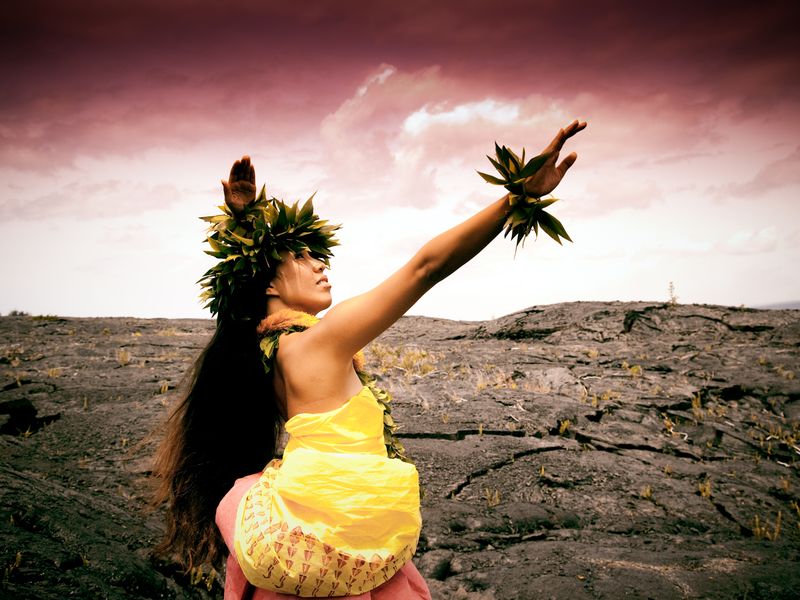 Woman in traditional hula dress in pose on lava field on the Big Island ...