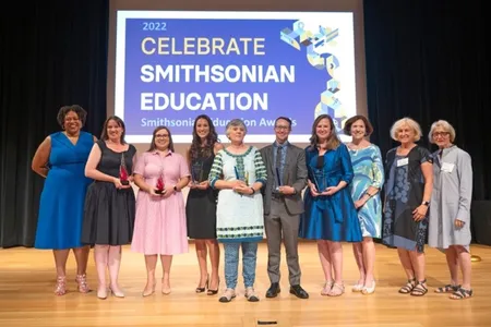 A group of people posing for a photo on a stage.  Dr. Monique M. Chism with Awardees and Smithsonian Women’s Committee supporters at the 2022 Smithsonian Education Awards Ceremony, July 28, 2022.