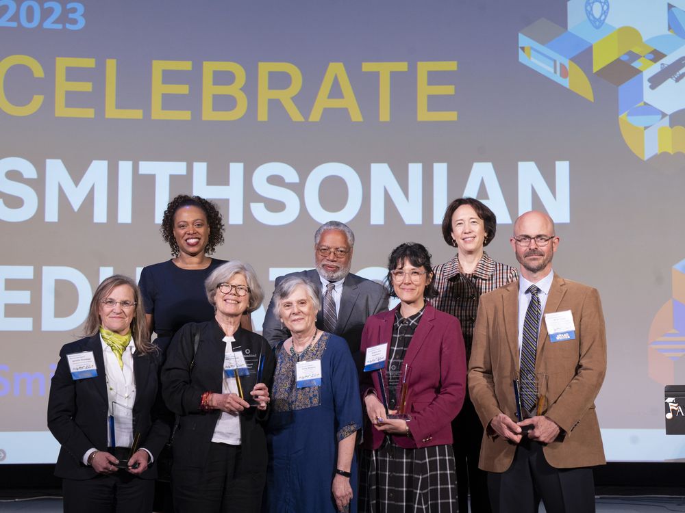 Group of Smithsonian Education awardees with leadership standing in front of a large screen that says "Celebrate Smithsonian Education"