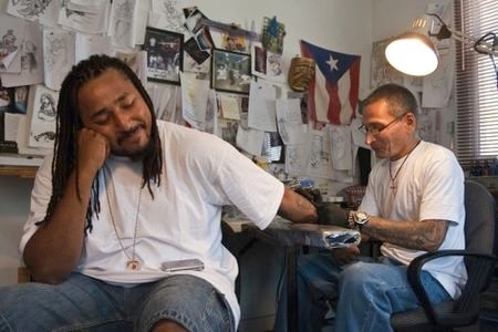 Q Monts sits patiently at Nu Flava Ink while tattoo artist Charles “Coco” Bayron puts the finishing touches on Q’s tattoo reading “Time is Money, Money is Time.”