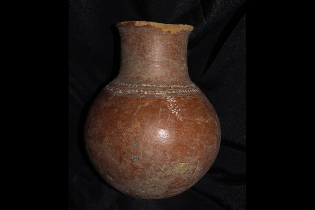 A reddish high-necked pot with some painting and visible cracks; mostly reddish-brown with specks of green and blue
