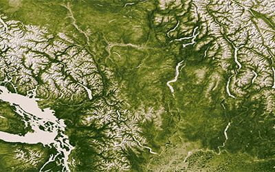Less conspicuous than the rugged Rocky, Cascade and Coast Mountain Ranges in this photograph are the markings of agriculture, in the bottom center.
