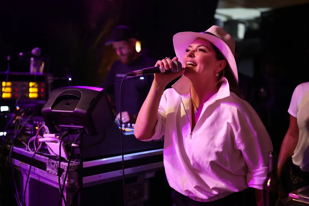 Shania Twain in a white shirt and hat singing on stage