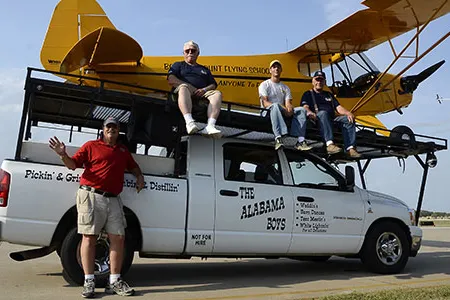 Pilot Greg Koontz (standing) flies an act that depends on the help of his Alabama Boys, Fred Masterson, Jason Hankins, and Walter Harvey (left to right, atop their mobile runway with Koontz’s Piper J-3 Cub).