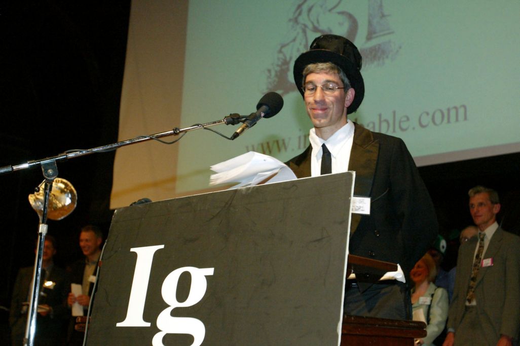 A man wearing a black suit and top hat stands at a podium